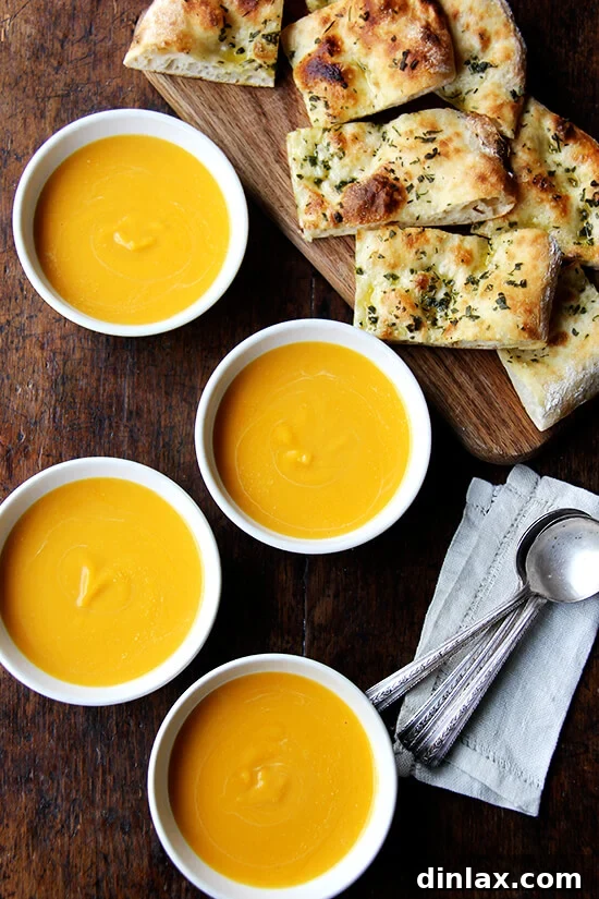 Two inviting bowls of butternut squash and cider soup, served alongside slices of golden herbed flatbread, ready for a delicious meal.