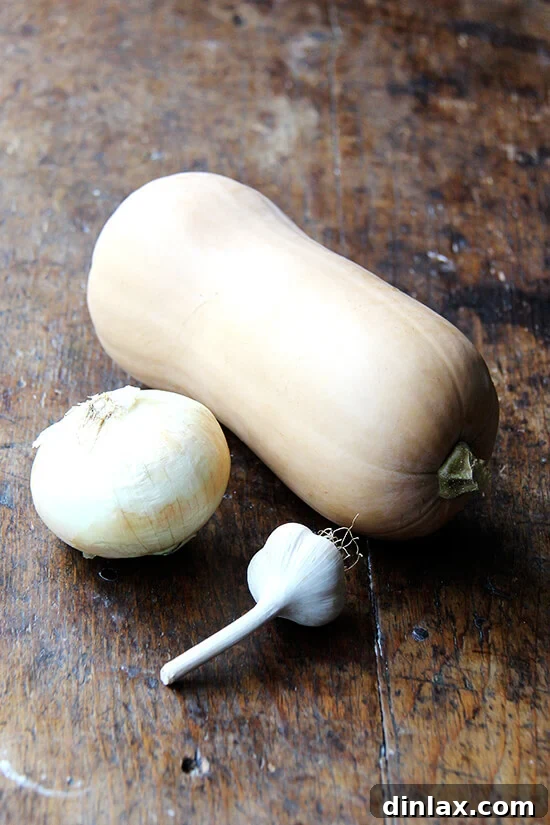 A beautiful arrangement of fresh butternut squash, a large onion, and a head of garlic on a wooden cutting board, ready for preparation.