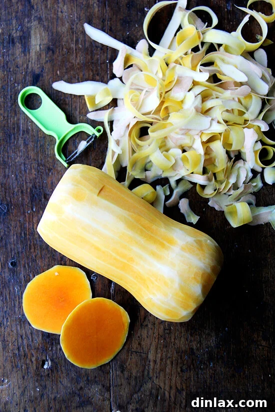 A perfectly peeled butternut squash stands alongside its trimmings, showcasing the preparation process.