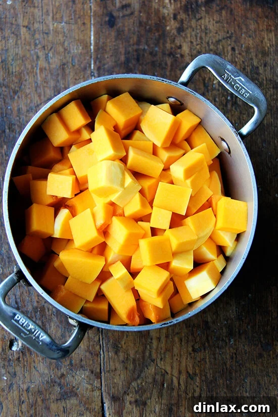 A soup pot now filled with vibrant orange cubes of butternut squash, layered over the softened aromatics.