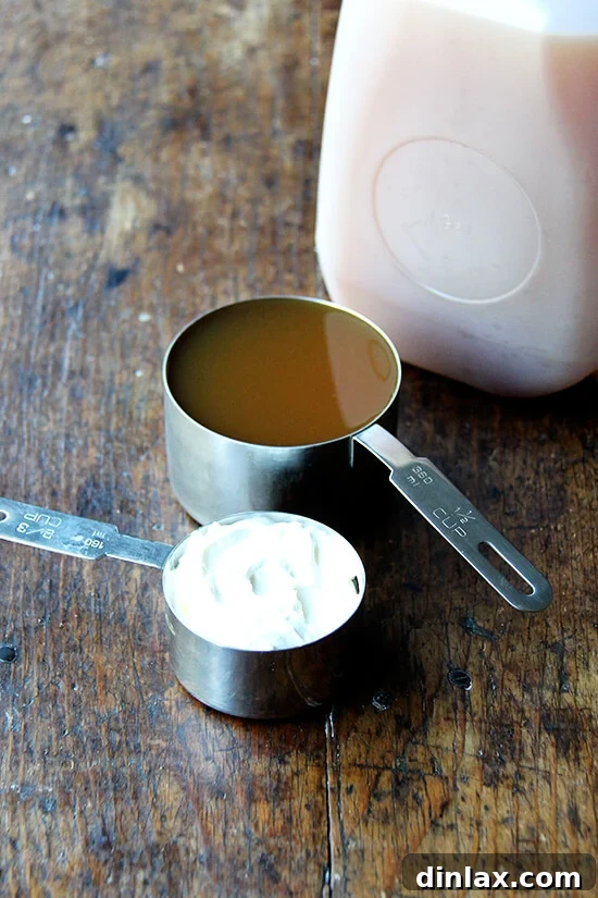 A clear measuring cup filled with golden apple cider stands next to a bowl of rich sour cream, poised to be added to the soup.