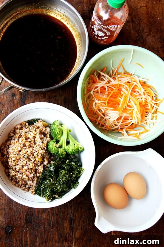 All essential components for a gourmet grain bowl laid out elegantly: a jar of homemade teriyaki sauce, a small bowl of bright quick-pickled carrots and daikon, a large bowl of re-steamed wheat berries, kale, and broccoli, and a dish of perfectly soft-boiled eggs.