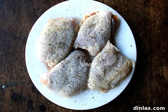 A plate of chicken thighs seasoned with salt and pepper, ready for cooking.