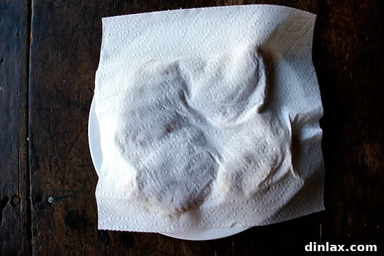 Chicken thighs on a plate, blotted with a paper towel for maximum crispiness.