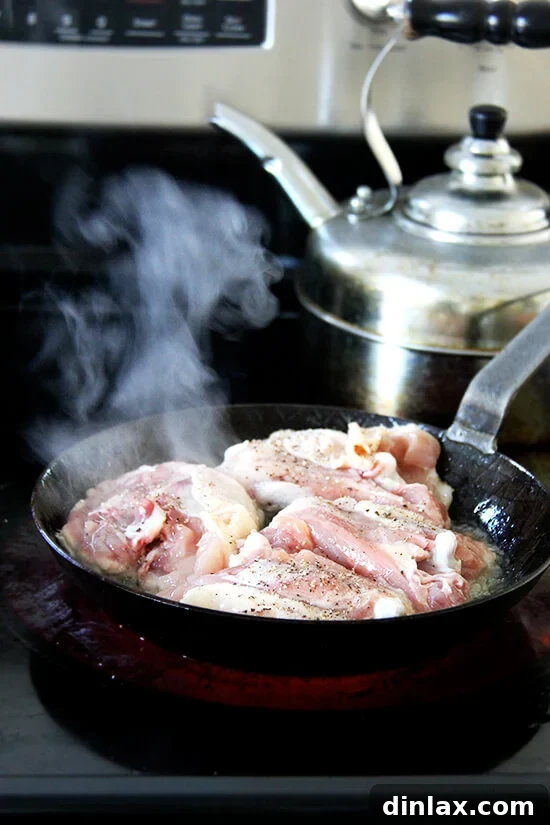 A skillet with chicken thighs actively cooking on the stovetop, developing a golden crust.