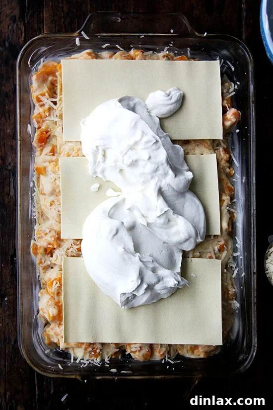 A 9x13-inch pan containing unbaked butternut squash lasagna topped with a creamy layer of whipped cream.