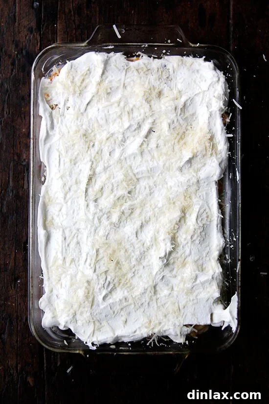 An unbaked butternut squash lasagna in a 9x13-inch pan, topped with Parmesan cheese, ready for the oven.