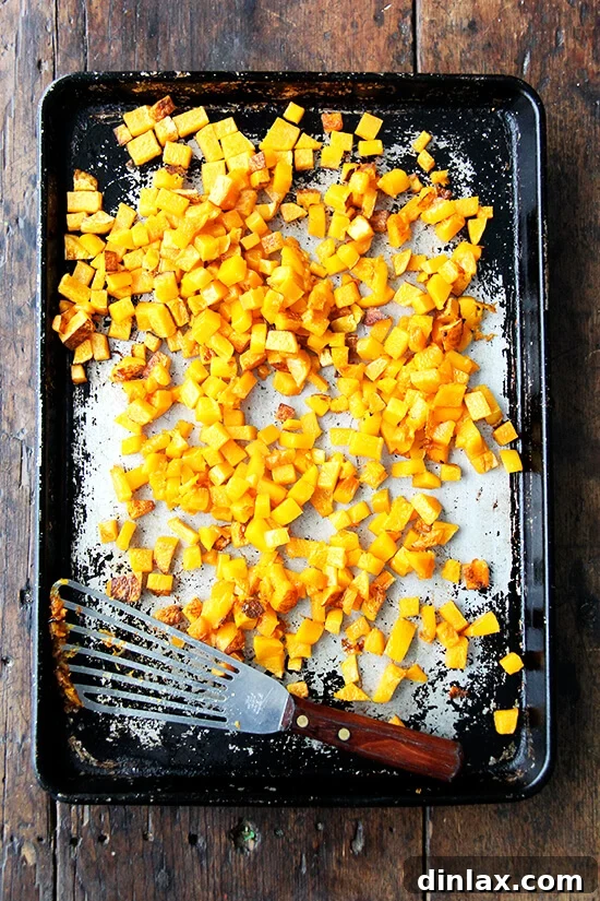 A rimmed sheet pan is covered with roasted butternut squash cubes, golden and slightly browned.