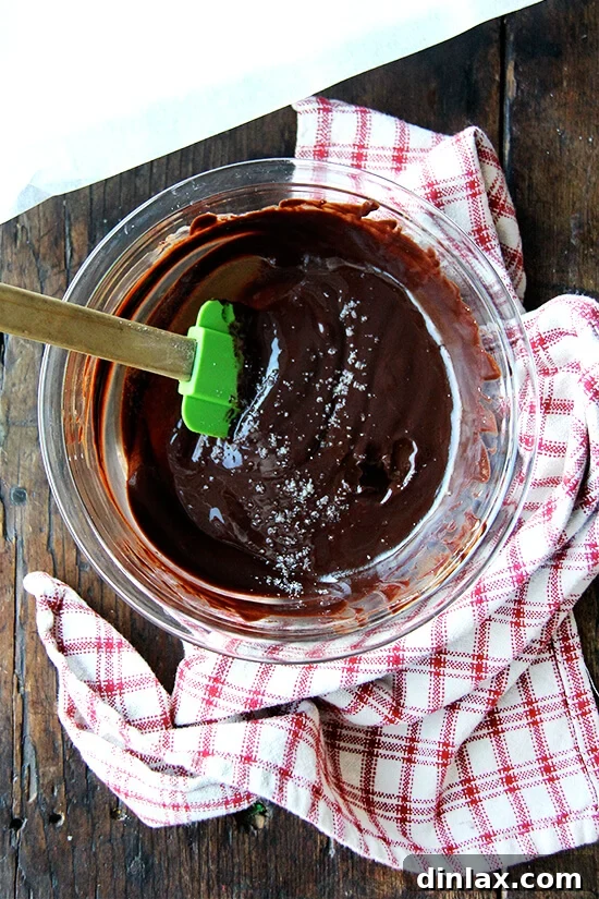 Decadent Grand Marnier Chocolate Truffles 5 A bowl filled with freshly melted chocolate ganache, glistening and smooth, with a pinch of flaky sea salt sprinkled on top and a spatula resting inside.