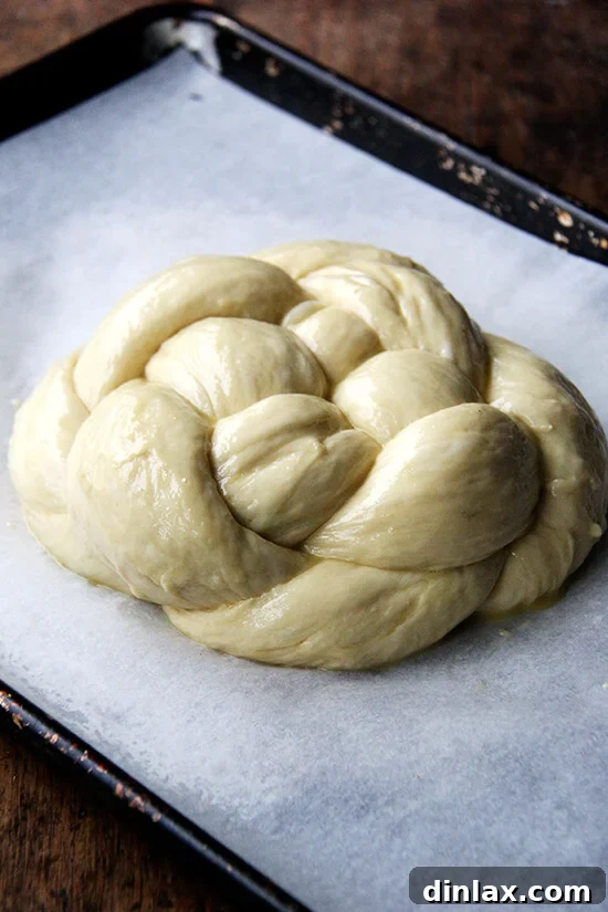 An egg-washed circular Challah bread on a parchment-lined sheet pan, prepared for baking.