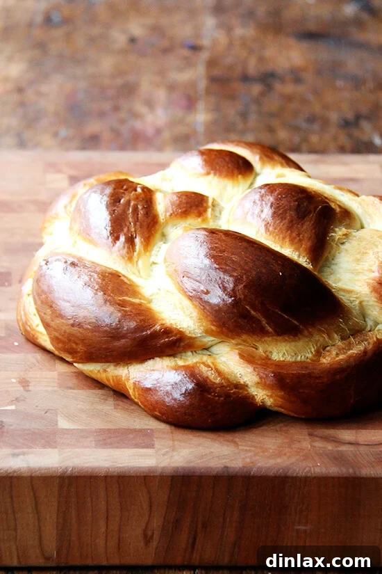 A beautifully braided loaf of homemade Challah bread on a wooden cutting board.