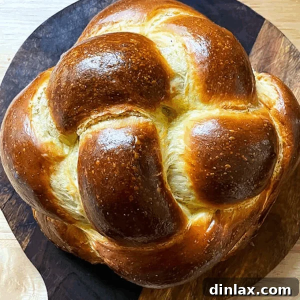 A perfectly braided loaf of Challah bread on a circular cutting board, ready to be sliced.