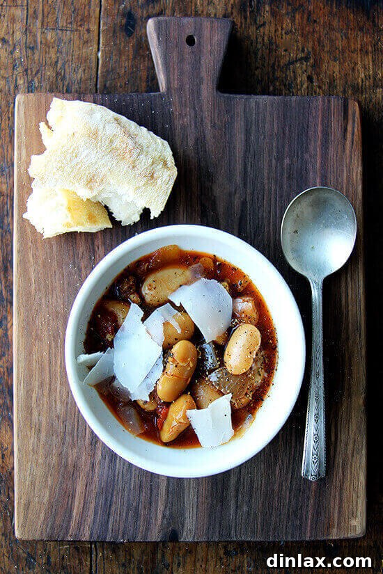 A rustic bowl of slow cooker large white beans (gigante beans), artfully arranged beside a hearty hunk of crusty bread, inviting a warm and satisfying meal.
