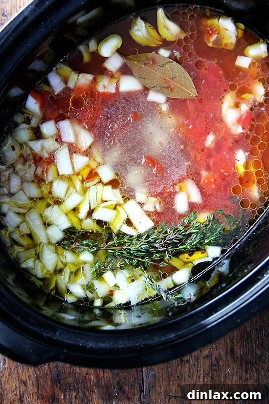 A slow cooker filled with the uncooked ingredients for white beans, featuring onions, herbs, and beans, poised to begin the long, slow cooking process.