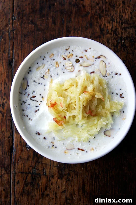 A bowl of Bircher muesli generously topped with a heap of freshly grated apple, showcasing a key ingredient for its signature flavor and texture.