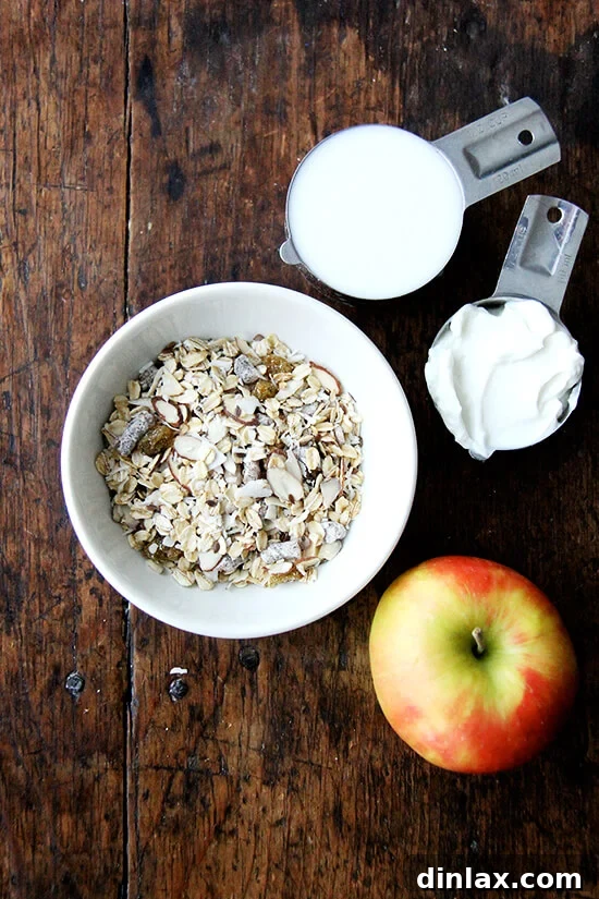 Individual ingredients for a single serving of Bircher muesli, including a bowl of muesli mix, milk, yogurt, and a grated apple, poised for combination.