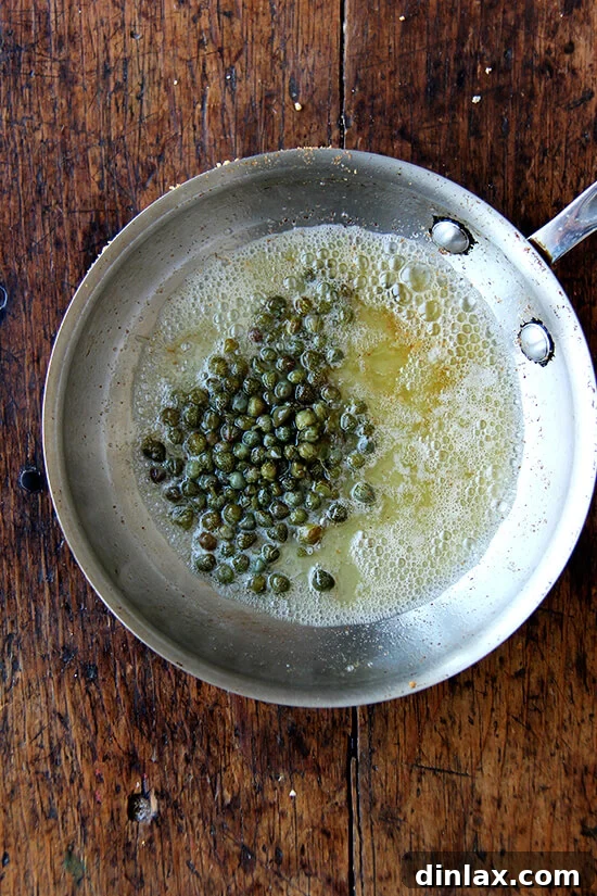 Capers frying in brown butter in a small pan, releasing their savory aroma.