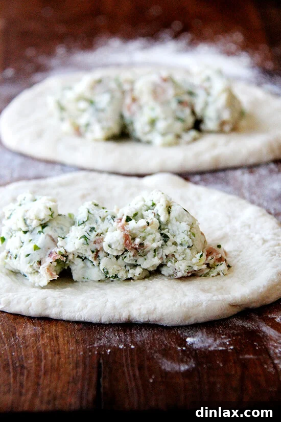 A few tablespoons of the rich and flavorful goat cheese and prosciutto filling are generously spread across each round of pizza dough, ready for folding.