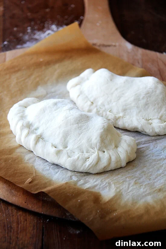 A perfectly folded and sealed calzone, ready for baking, showcasing the crimped edges that keep the cheesy filling securely inside.