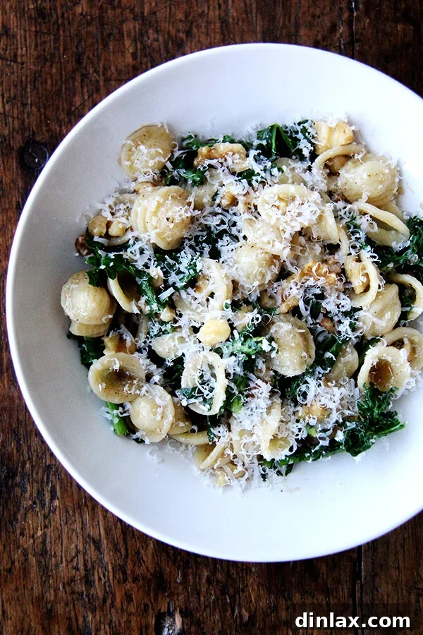 A perfectly plated bowl of orecchiette pasta with Swiss chard, glossy brown butter, and crunchy walnuts, garnished with fresh cheese.