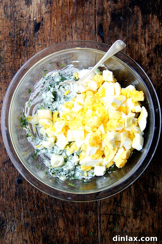 Briny Egg Salad Crostini 5 Coarsely chopped pickled hard-boiled eggs being folded into the prepared mayonnaise and herb dressing in a mixing bowl, creating the final egg salad texture.
