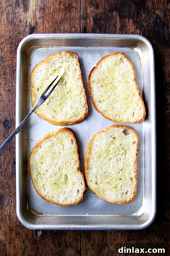 Briny Egg Salad Crostini 9 A hand gently rubbing a freshly toasted slice of bread with a cut garlic clove, infusing it with aromatic flavor.