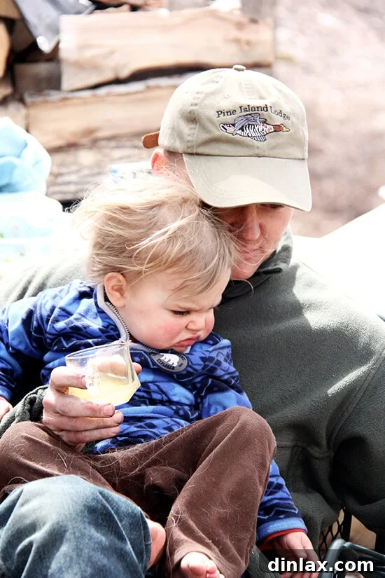 Children Wren and Ben enthusiastically taking turns rotating the kokoretsi on the spit, learning family traditions.