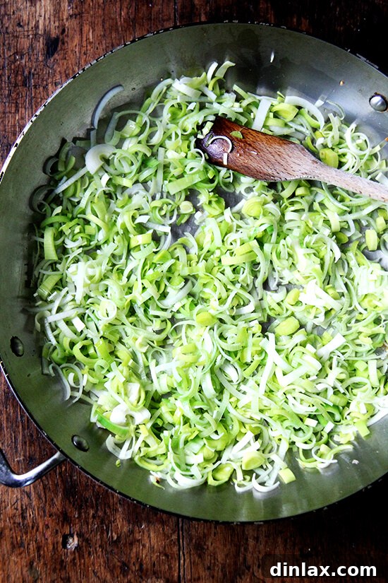 Tender sliced leeks being added to the sauté pan, ready to cook down.