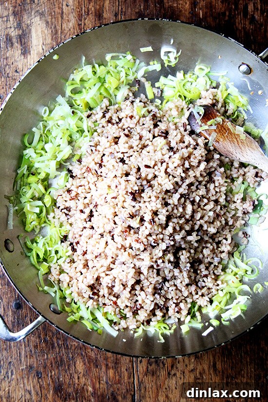 Cooked rice being added to the pan with sautéed leeks, ready to be stir-fried and combined.