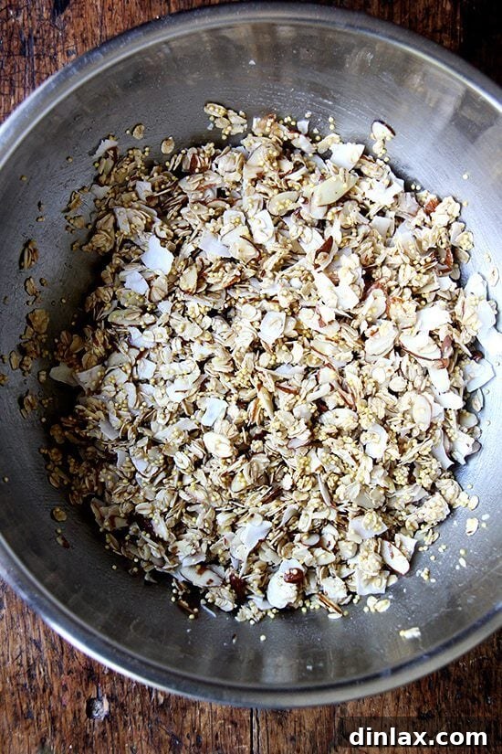 Granola mixture ready for the oven, spread evenly on a parchment-lined sheet.