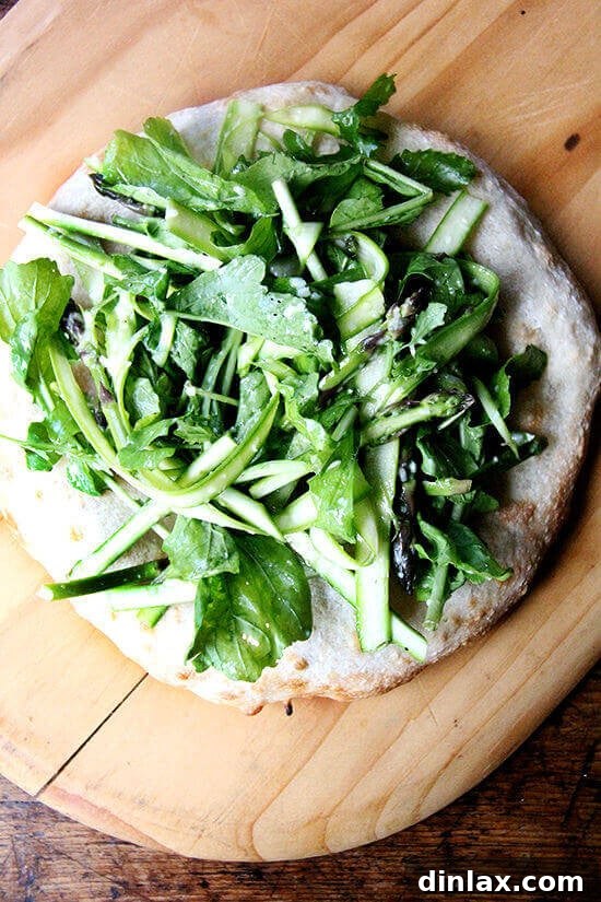 This shaved asparagus arugula salad makes a lovely side dish on its own, but can easily be turned into a filling and delicious meal: Simply heap it atop an enormous carbohydrate—pizza, flatbread, bruschetta. There’s no science behind that. // alexandracooks.com Shaved asparagus and arugula salad piled high on a piece of golden flatbread.