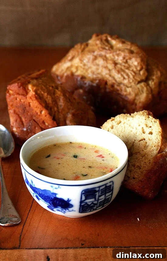 Hearty Vermont Cheddar Cheese Soup served with warm beer bread, perfect for a cozy winter meal. Features rich cheddar, aromatic thyme, and savory pancetta, alongside a vibrant salad of arugula, candied pecans, pear, and blue cheese.