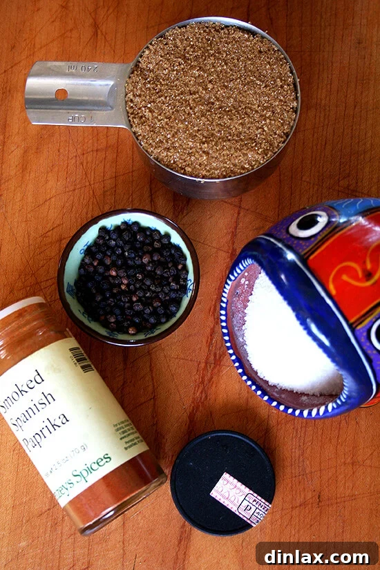 A selection of four essential spices: kosher salt, black pepper, brown sugar, and smoked paprika, arranged on a rustic wooden surface, ready for seasoning baby back ribs.