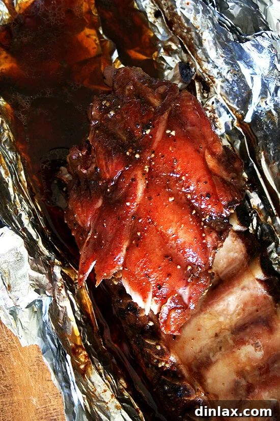 A close-up, overhead view of succulent baby back ribs, beautifully caramelized and glistening with juices, still nestled in their foil wrapping, ready for serving after being finished under the broiler.