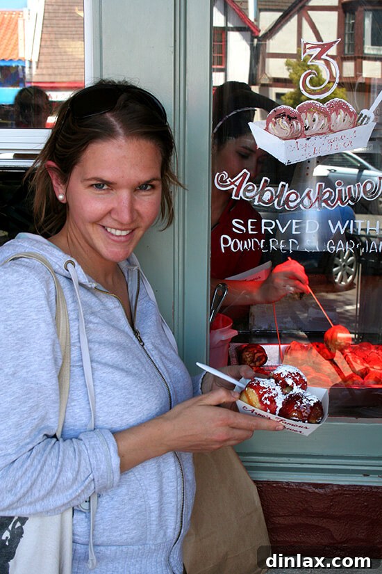 A vibrant close-up of delicious Arne's Aebleskivers, Danish pancake balls, generously drizzled with glistening raspberry jam and a dusting of white powdered sugar.