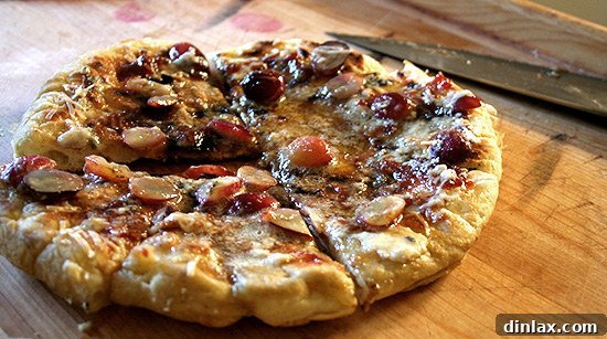 A savory homemade grilled flatbread generously topped with fresh green grapes and bubbling melted cheese, a rustic and delicious creation.