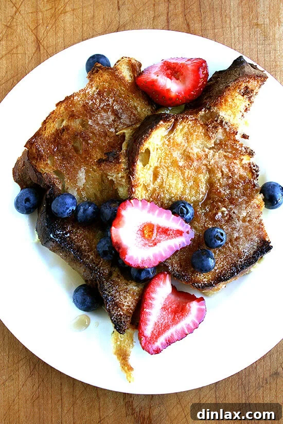 A plate of overnight French toast topped with fresh berries, powdered sugar, and a drizzle of maple syrup.