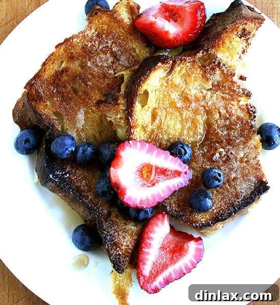 A plate of overnight French Toast with berries, powdered sugar, and maple syrup.
