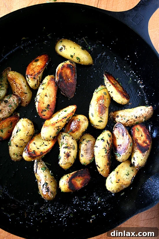A cast iron skillet filled with golden-brown, crispy fingerling potatoes, garnished with fresh herbs.
