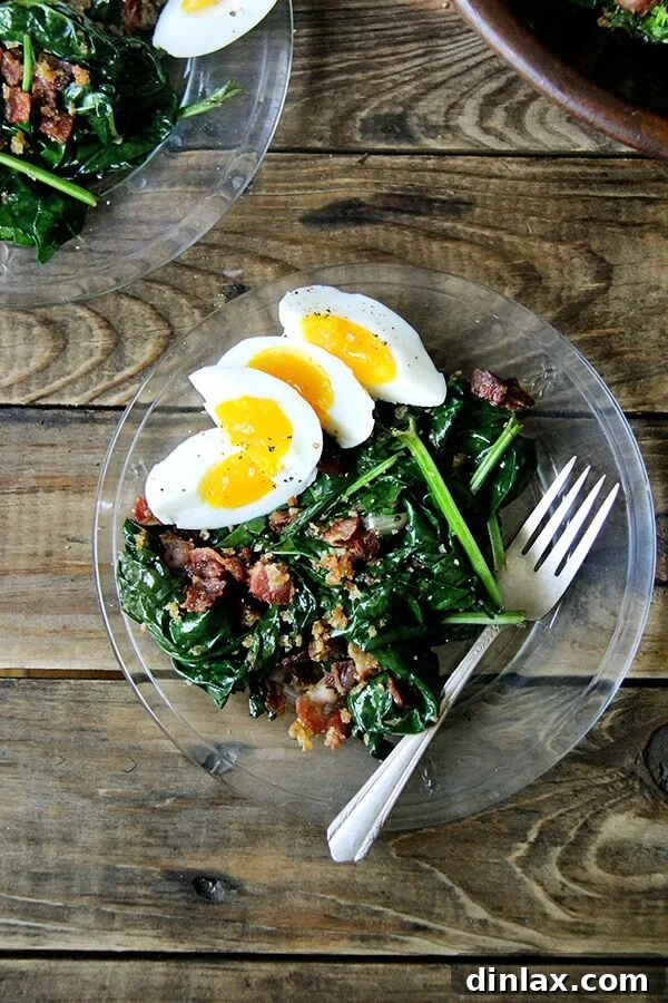 Alice Waters' Signature Warm Spinach Salad 4 A close-up of warm spinach salad with bacon and bread crumbs on a pristine white plate, garnished with soft-boiled egg quarters.