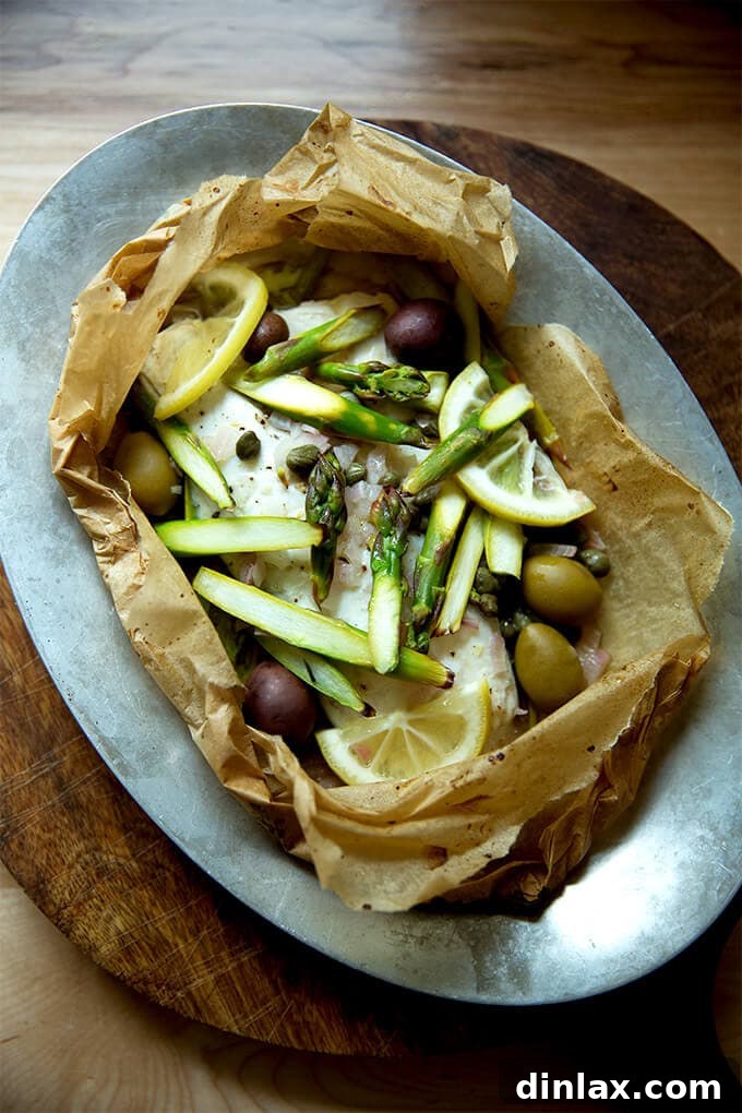 A sizzle pan with an opened fish en papillote, revealing perfectly cooked fish and vibrant vegetables inside the parchment packet.