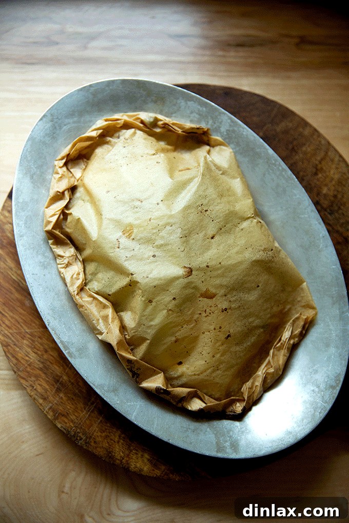 A sizzle pan featuring a batch of freshly baked fish en papillote, just removed from the oven, with the parchment packets still visibly puffed and steaming.