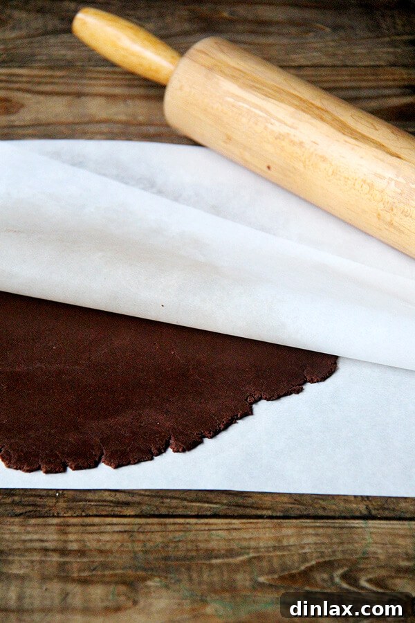 Rolling out the rich chocolate TKO dough between parchment paper for even thickness, essential for perfect homemade cookies.