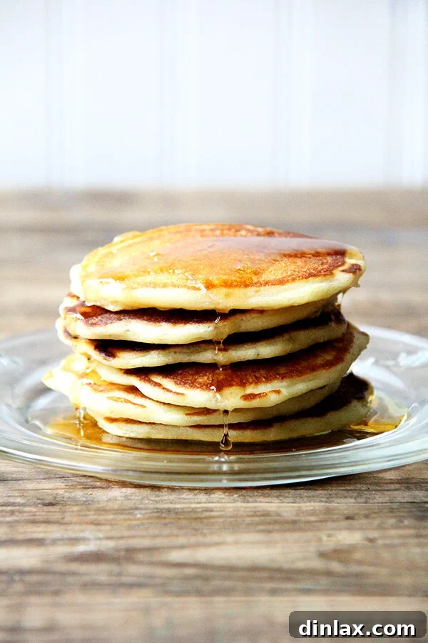 A tall stack of golden brown one-bowl buttermilk pancakes, drizzled with syrup and topped with fresh berries.