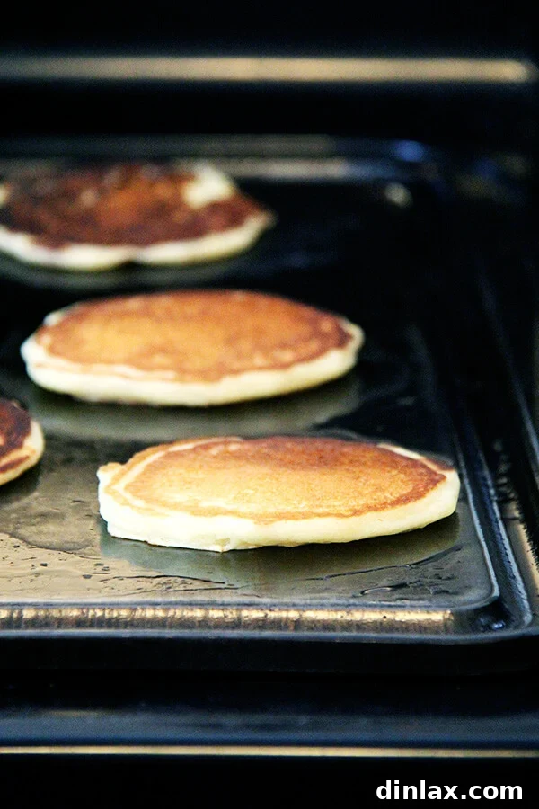 One-bowl buttermilk pancakes cooking on a griddle, visibly puffing up.