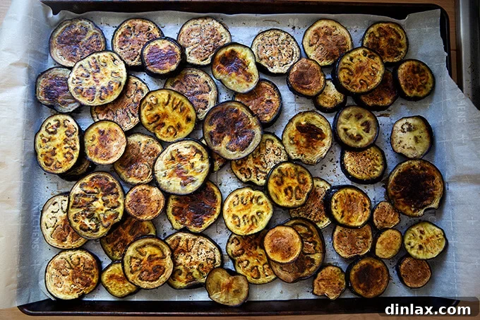 Roasted eggplant slices, golden brown and slightly caramelized, arranged on a baking sheet.