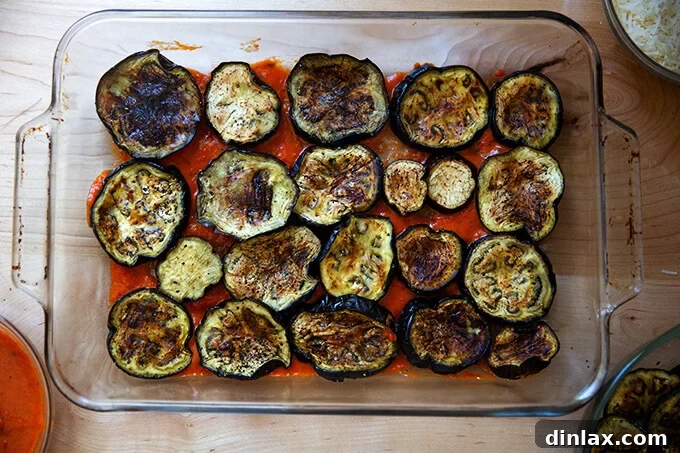 A 9x13-inch baking pan with an initial layer of tomato sauce and roasted eggplant slices.