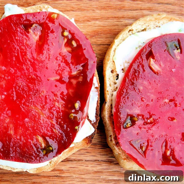 A perfectly assembled toasted sesame bagel with chive cream cheese, a thick slice of heirloom tomato, and a sprinkle of sea salt