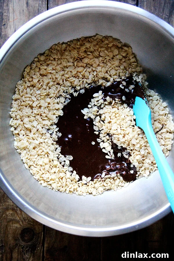 Crispy rice cereal being generously coated with the warm, gooey syrup and chocolate mixture in a large bowl, ensuring every piece is covered.