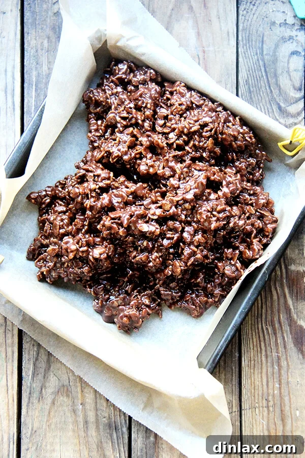 The sticky crispy treat mixture being meticulously pressed into a parchment-lined baking pan, forming an even and compact layer.
